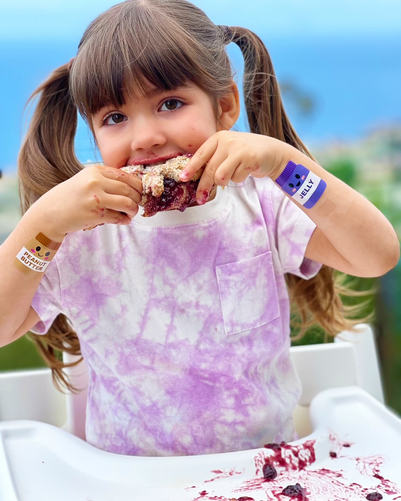 Load image into Gallery viewer, Young girl eating a peanut butter and jelly sandwich wearing Boo Boo Buddies Bandages
