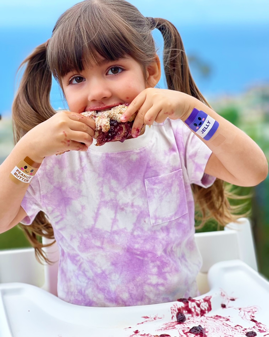 Young girl eating a peanut butter and jelly sandwich wearing Boo Boo Buddies Bandages